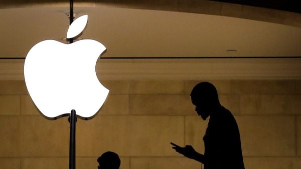 A man in shadow looks at his mobile device near a lit up Apple logo.