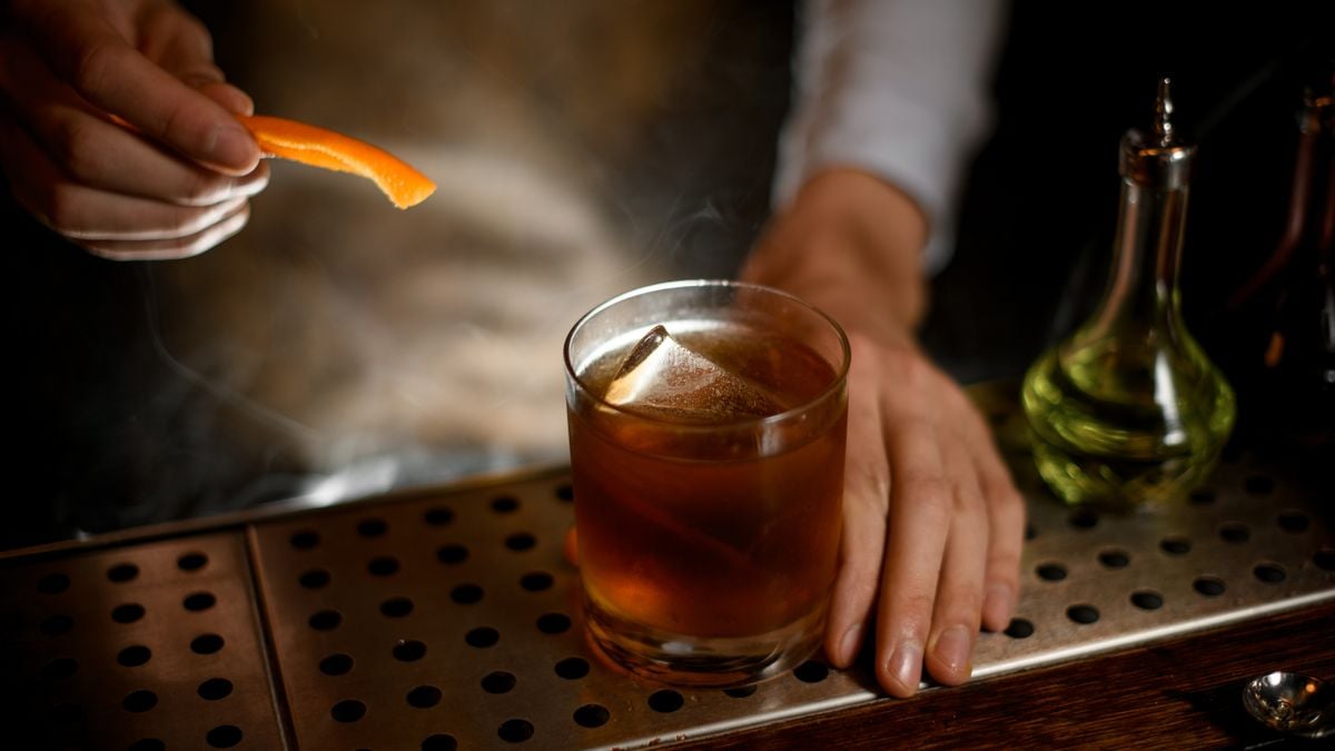 A bartender adds an orange peel to a whiskey drink with ice.