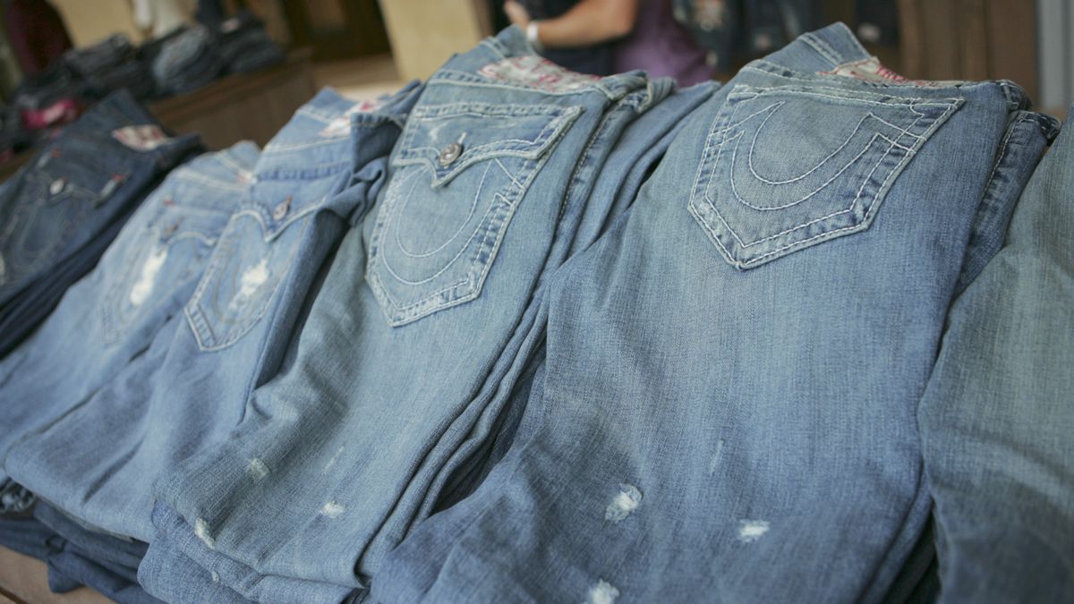 A stack of lightly distressed denim jeans with horseshoe stitching on the back pockets,