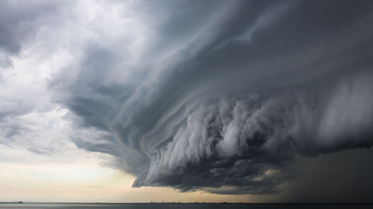 A massive gray storm cloud gathers on the horizon over a placid body of water.
