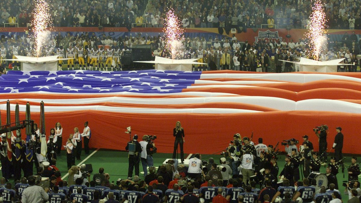 An American flag is unfurled over a football field as fireworks go off.