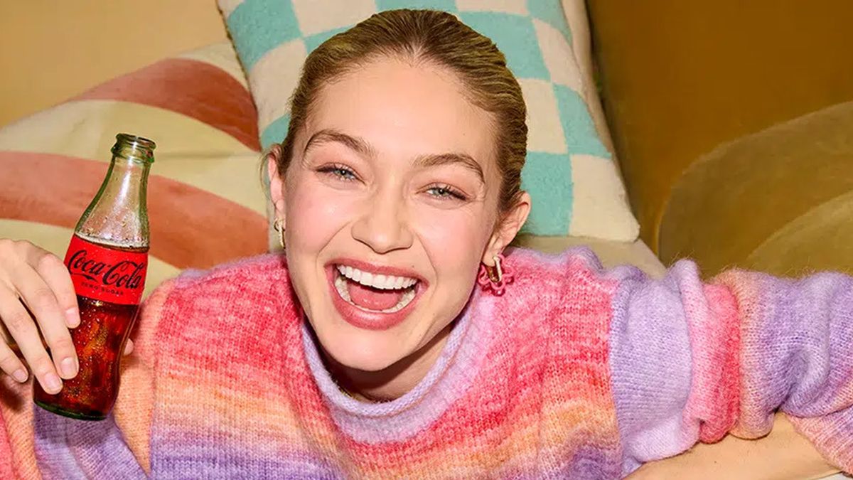 Gigi Hadid holds a bottle of Coke while wearing a colorful sweater.