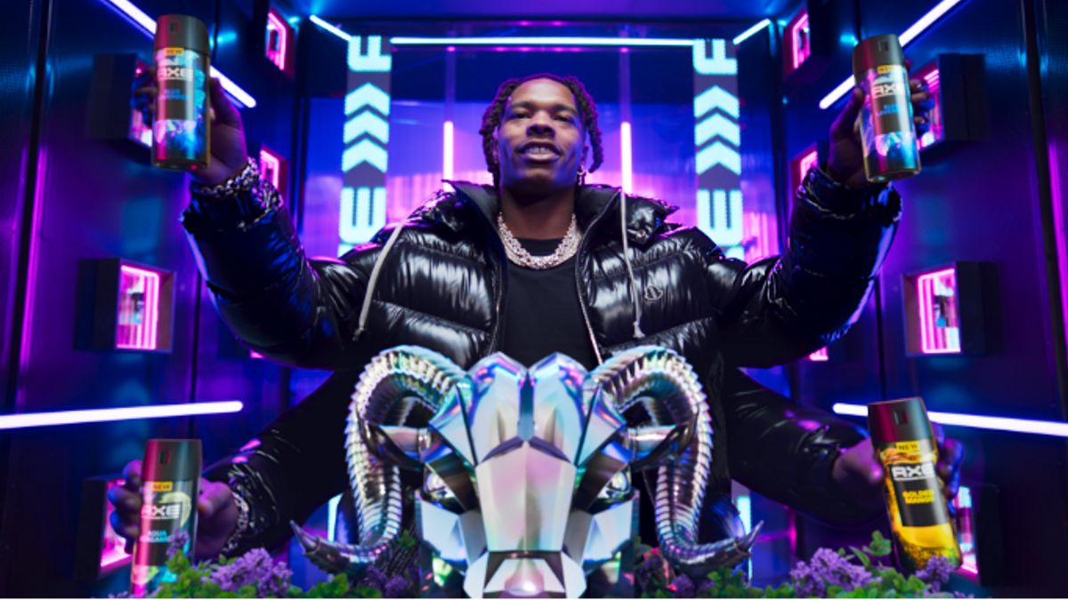 Rapper Lil Baby behind the metal head of a goat with four arms each holding a different fragrance.