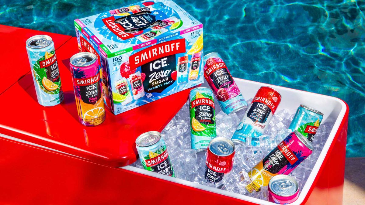 Cans of Smirnoff Ice sit in a red cooler next to blue water.